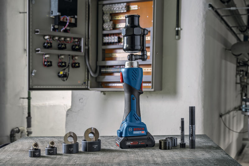 Kabelloses hydraulisches Stanzwerkzeug mit verschiedenen Aufsätzen, platziert in der Nähe eines offenen Bedienfelds. Anwendungsbild