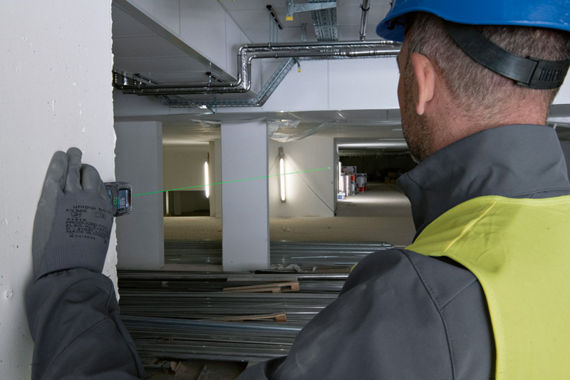 Eine Person mit Sicherheitsausrüstung verwendet ein Lasermessgerät, um die Entfernung auf einer Baustelle zu überprüfen. Anwendungsbild