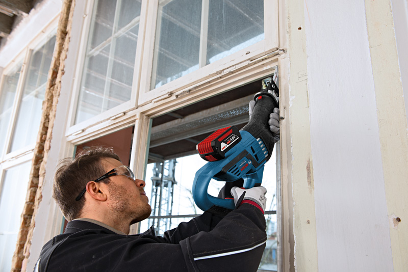 Eine Person mit Sicherheitsausrüstung schneidet mit einer Säbelsäge einen Fensterrahmen durch. Anwendungsbild