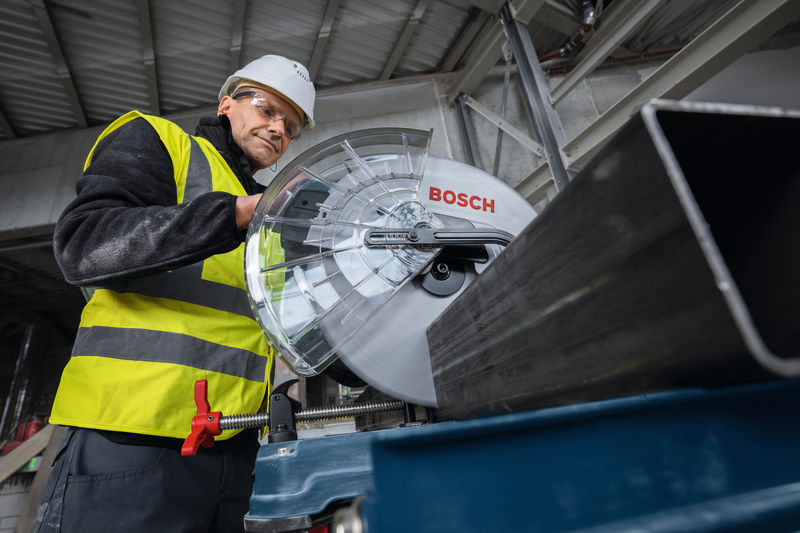 Eine Person mit Schutzausrüstung schneidet mit einer großen Metalltrennsäge einen Metallträger durch. Anwendungsbild