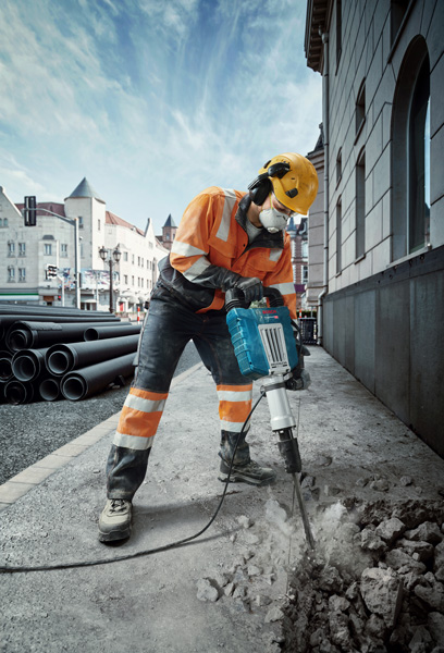 Eine Person mit Sicherheitsausrüstung bricht mit einem Aufbrechhammer den Bürgersteig einer Stadtstraße auf. Anwendungsbild