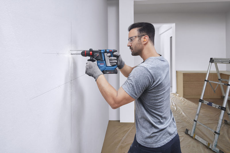 Eine Person mit Schutzausrüstung bohrt mit einem Akku-Bohrhammer in eine markierte Wand. Anwendungsbild