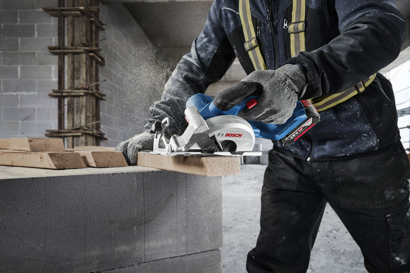 Eine Person mit Sicherheitsausrüstung schneidet auf einer Baustelle mit einer Kreissäge Holz. Anwendungsbild