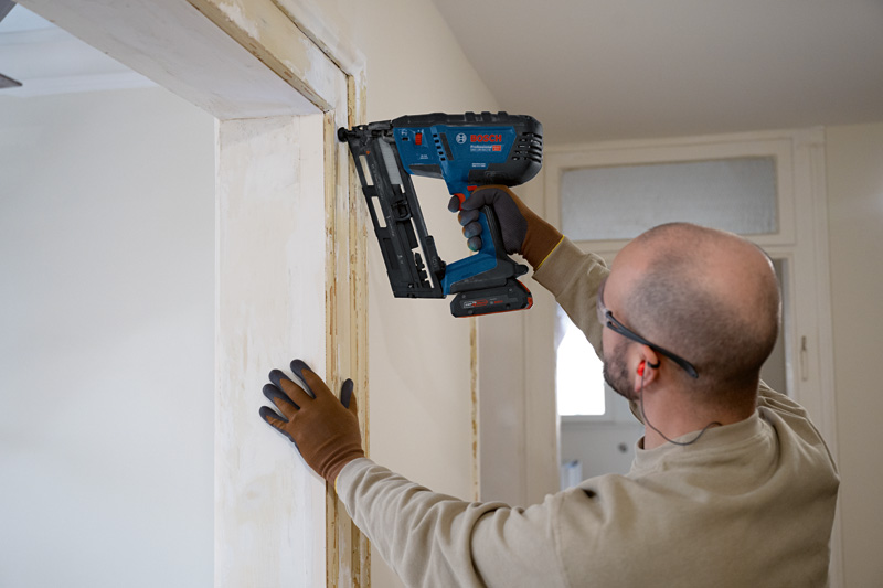 Person mit Sicherheitsausrüstung, die Holzverkleidungen mit einem Akkunagler anbringt. Anwendungsbild