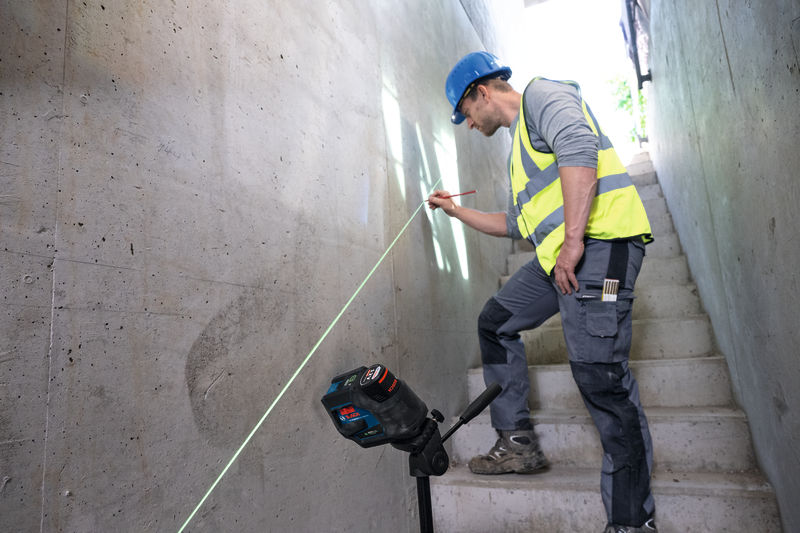 Eine Person mit Sicherheitsausrüstung markiert mithilfe eines Lasernivelliergeräts eine Linie auf einer Betontreppe. Anwendungsbild