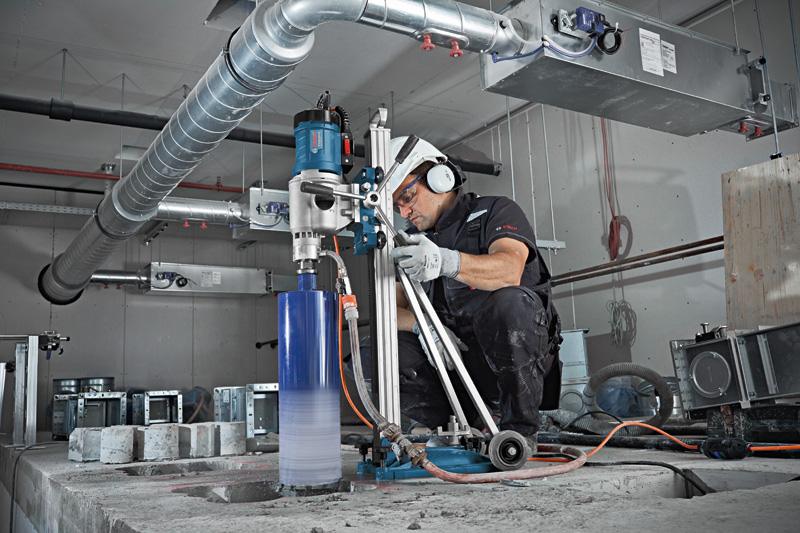 Eine Person mit Sicherheitsausrüstung bedient eine Kernbohrmaschine auf einem Betonboden. Anwendungsbild