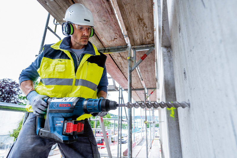 Eine Person mit Schutzausrüstung bohrt mit einem Akku-Bohrhammer in Beton. Anwendungsbild
