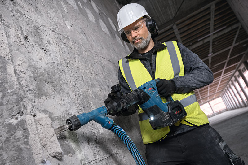 Eine Person mit Sicherheitsausrüstung verwendet einen Akku-Abbruchhammer, um Beton aufzubrechen. Anwendungsbild