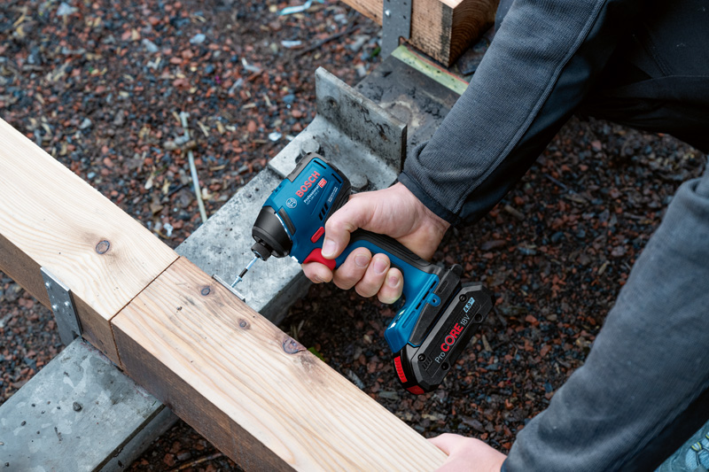 Eine Person schraubt mit einem Akku-Schlagschrauber eine Schraube in einen Holzbalken. Anwendungsbild