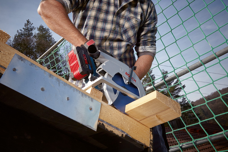 Eine Person schneidet auf einer Baustelle einen Holzbalken mit einer Kreissäge. Anwendungsbild