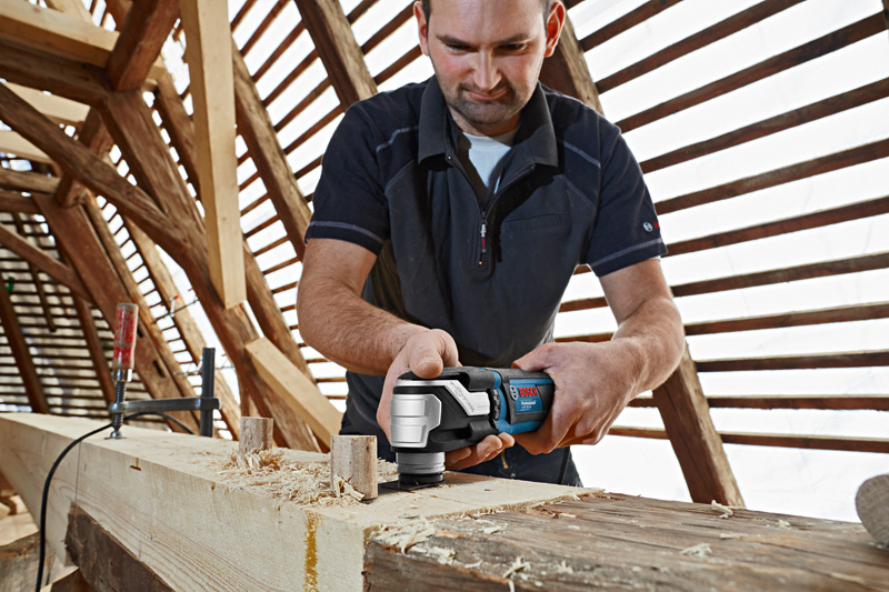 Eine Person formt in einer Werkstatt einen Holzbalken mit einem Mehrzweckwerkzeug. Anwendungsbild