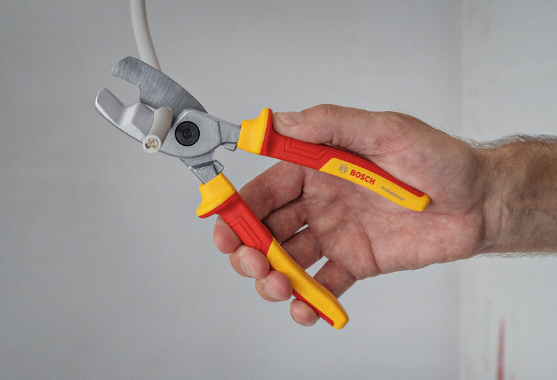 Eine Person schneidet ein Elektrokabel mit einer isolierten Zange durch. Anwendungsbild