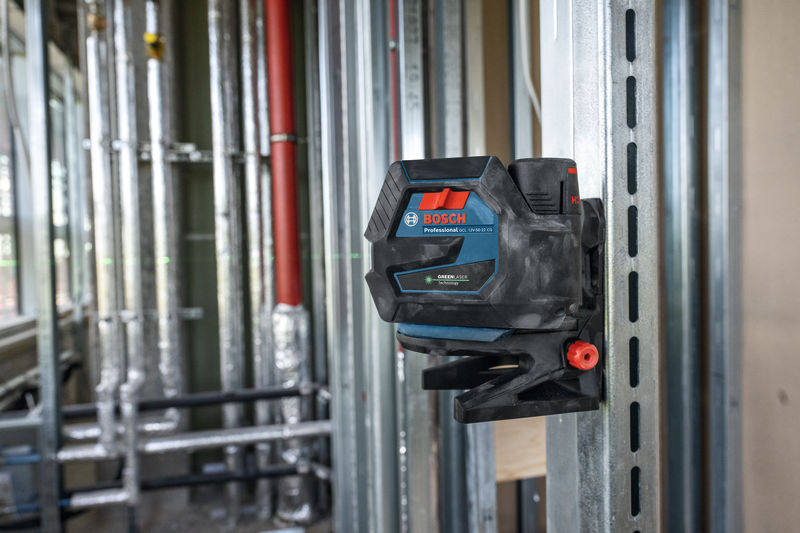 Ein auf einem Metallbolzen montiertes Lasernivelliergerät projiziert grüne Linien über eine Baustelle. Anwendungsbild