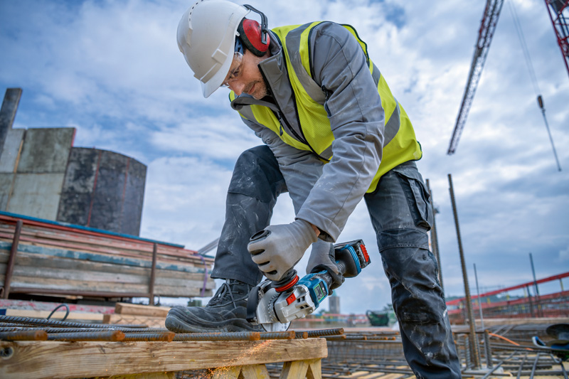 Eine Person mit Sicherheitsausrüstung schneidet auf einer Baustelle Bewehrungsstahl mit einem Akku-Winkelschleifer. Anwendungsbild