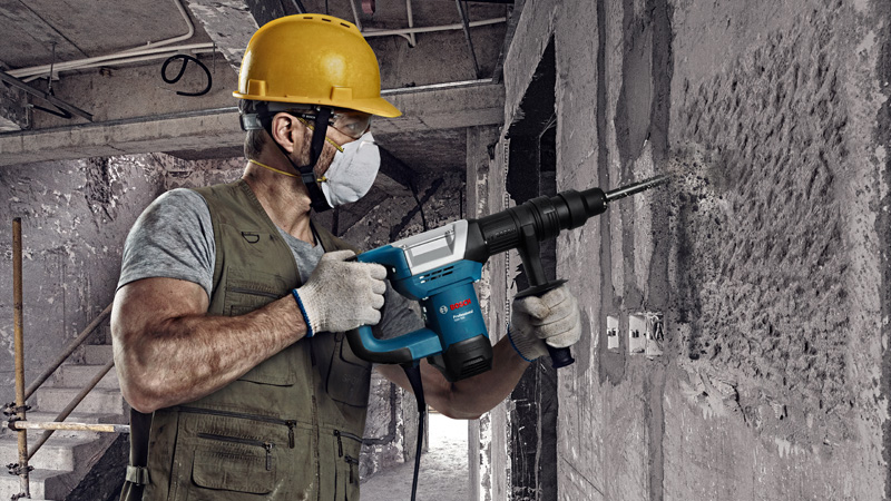 Eine Person mit Sicherheitsausrüstung benutzt einen Abbruchhammer, um eine Betonwand einzubrechen. Anwendungsbild