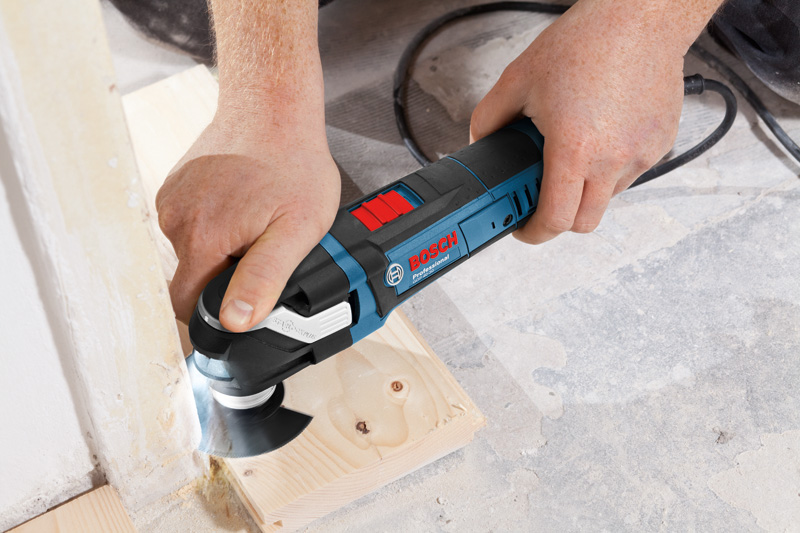 Eine Person schneidet mit einem Multischneider-Elektrowerkzeug Holz am Boden. Anwendungsbild