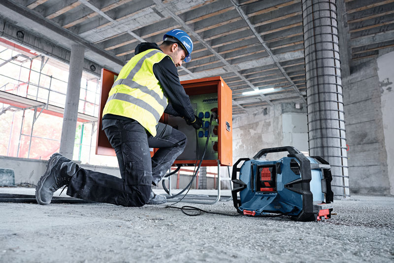 Eine Person mit Sicherheitsausrüstung schließt auf einer Baustelle Kabel an einen Schaltschrank an. Anwendungsbild