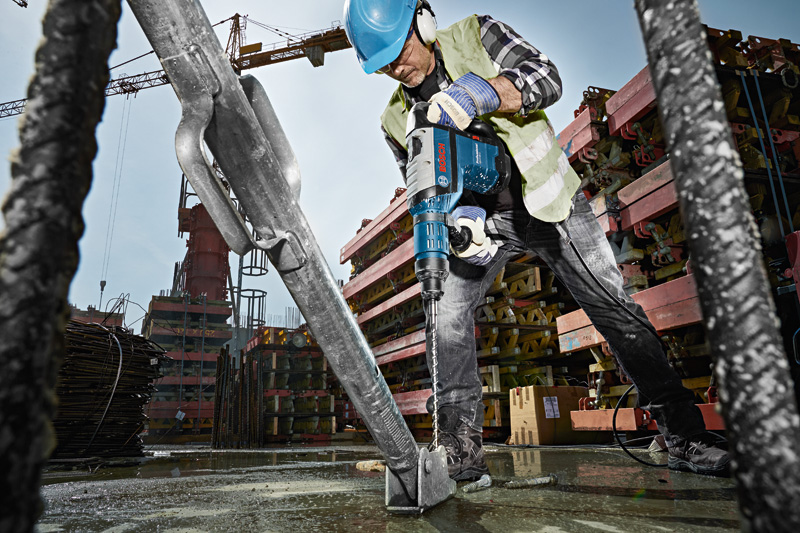 Ein Arbeiter mit Sicherheitsausrüstung bohrt mit einem Bohrhammer in ein Betonfundament auf einer Baustelle. Anwendungsbild