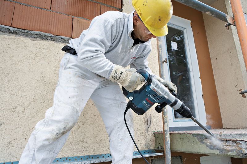 Eine Person mit Sicherheitsausrüstung verwendet einen Bohrhammer, um auf einer Baustelle Beton aufzubrechen. Anwendungsbild