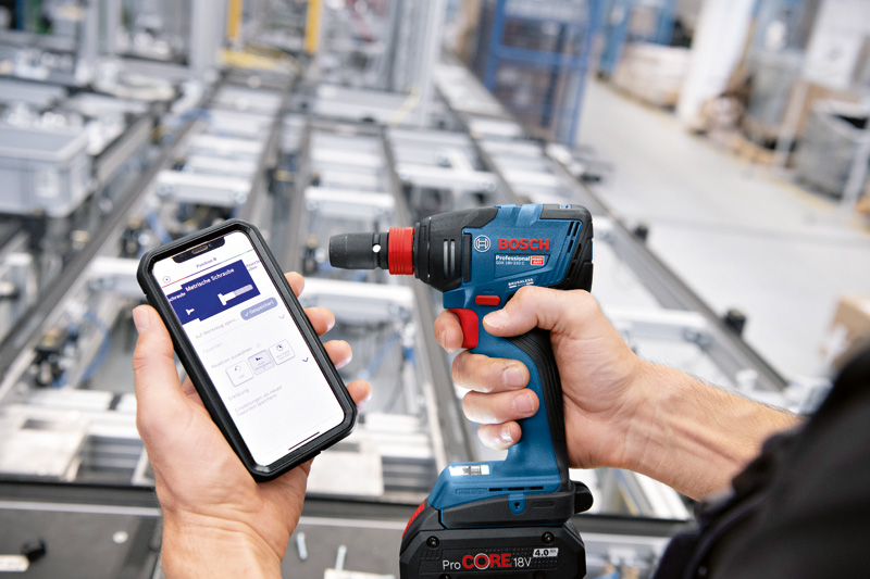 Eine Person steuert in einer industriellen Umgebung eine Akkubohrmaschine über ein Smartphone. Anwendungsbild