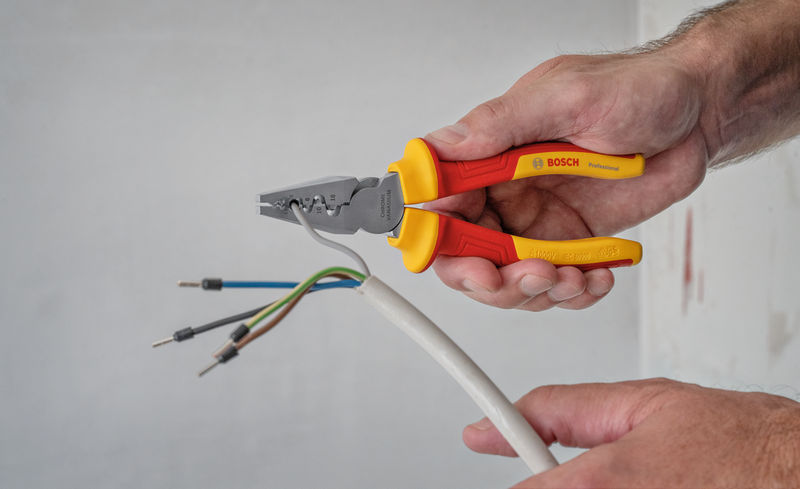 Eine Person entfernt die Isolierung von elektrischen Leitungen mithilfe einer isolierten Zange. Anwendungsbild