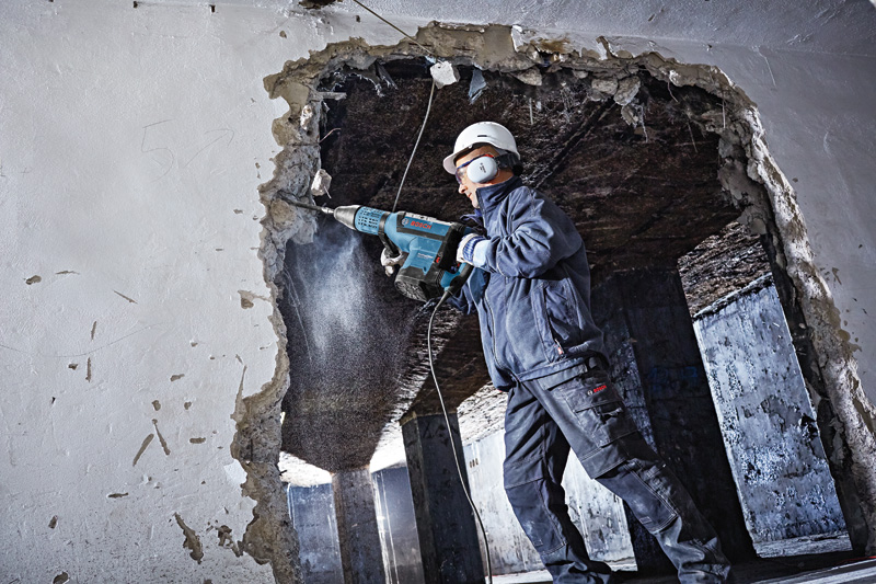 Eine Person mit Schutzausrüstung durchbricht mit einem Bohrhammer eine Betonwand. Anwendungsbild