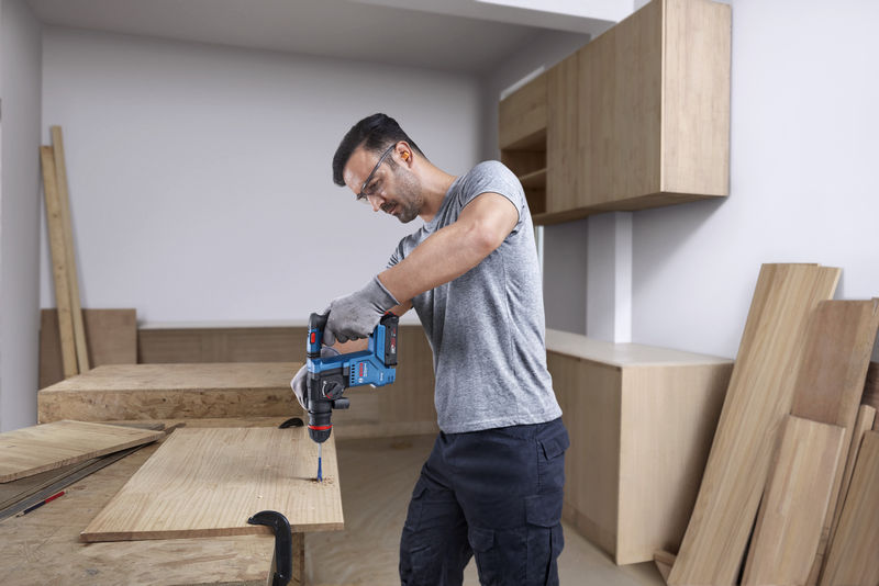 Eine Person mit Schutzausrüstung bohrt mit einem Akku-Bohrhammer in Holz. Anwendungsbild