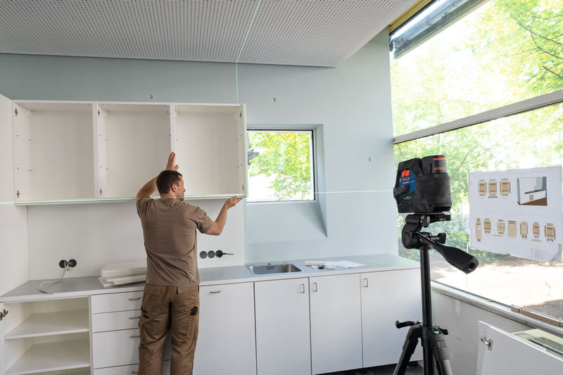 Eine Person richtet Küchenschränke mithilfe eines auf einem Stativ montierten Lasernivelliergeräts aus. Anwendungsbild