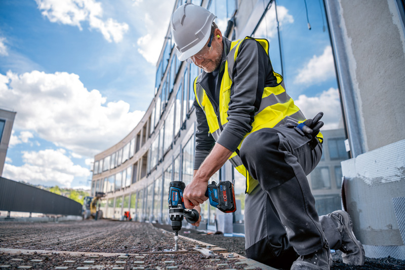 Eine Person mit Sicherheitsausrüstung verwendet einen Akku-Bohrschrauber auf einer Baustelle. Anwendungsbild