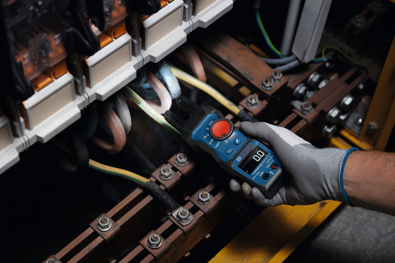 Eine Person mit Sicherheitsausrüstung testet mit einem Gabelmessgerät elektrische Leitungen in einem Panel. Anwendungsbild