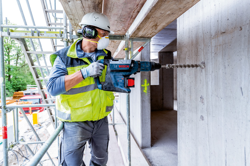 Eine Person mit Schutzausrüstung bohrt mit einem Akku-Bohrhammer in Beton. Anwendungsbild