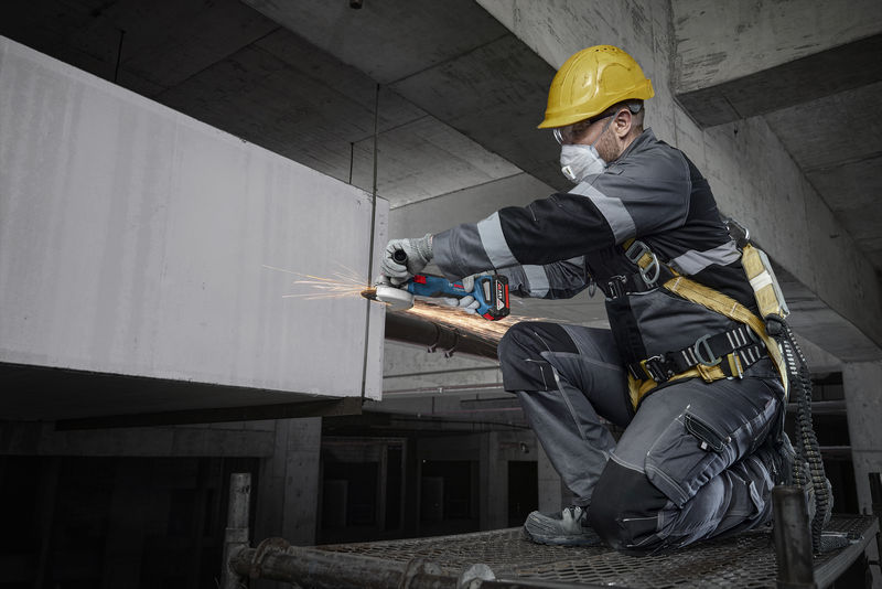 Eine Person mit Sicherheitsausrüstung schleift auf einer Baustelle Metall. Anwendungsbild