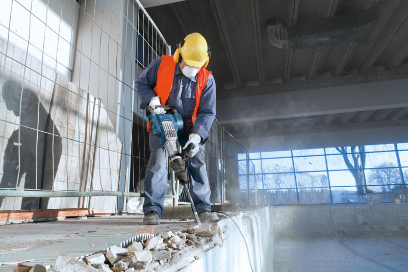 Eine Person mit Sicherheitsausrüstung verwendet einen Abbruchhammer, um Beton in Innenräumen aufzubrechen. Anwendungsbild
