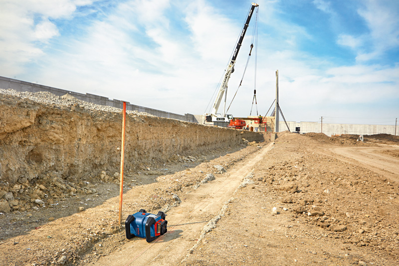 Lasernivellierungswerkzeug auf einer Baustelle mit einem Kran, der im Hintergrund Materialien hebt. Anwendungsbild