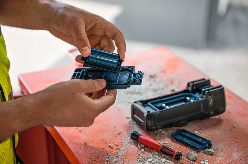 Eine Person mit Schutzausrüstung wechselt auf einer staubigen Werkbank die Batterien eines Elektrowerkzeugs. Anwendungsbild