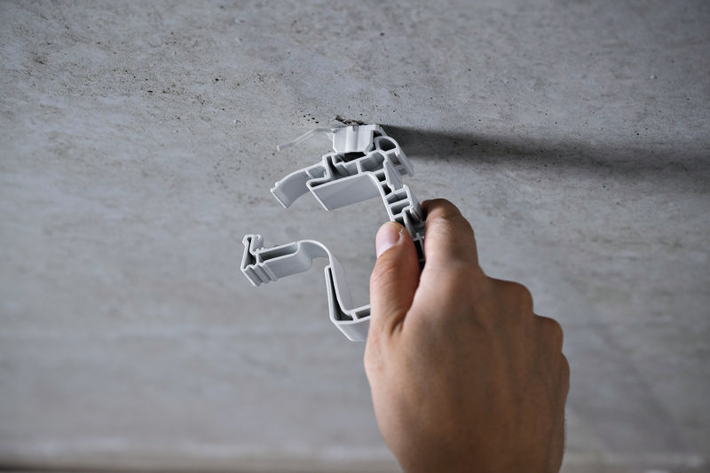 Eine Person installiert eine Montagehalterung aus Kunststoff an einer Betondecke. Anwendungsbild