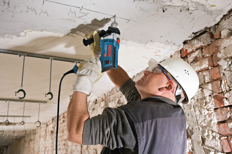 Eine Person mit Schutzausrüstung bohrt mit einer Schlagbohrmaschine in eine Betondecke. Anwendungsbild