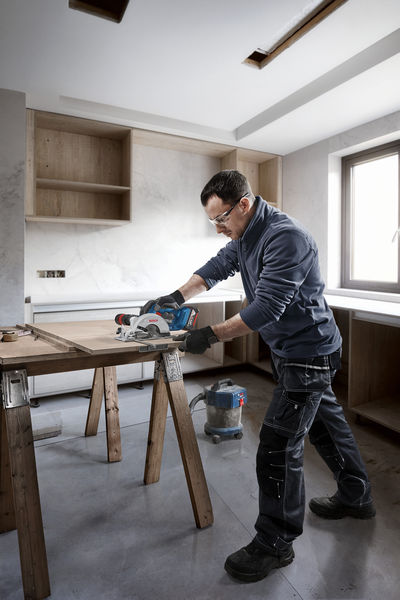 Eine Person mit Sicherheitsausrüstung schneidet mit einer Kreissäge Holz auf einem Tisch. Anwendungsbild