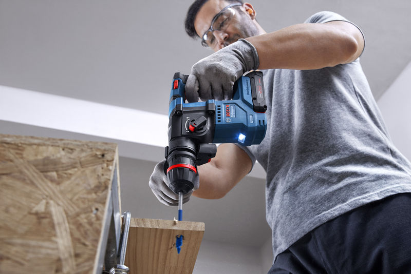 Eine Person mit Schutzausrüstung bohrt mit einem Akku-Bohrhammer in Holz. Anwendungsbild
