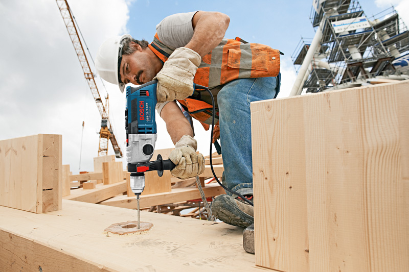 Eine Person mit Sicherheitsausrüstung bohrt auf einer Baustelle in Holz. Anwendungsbild