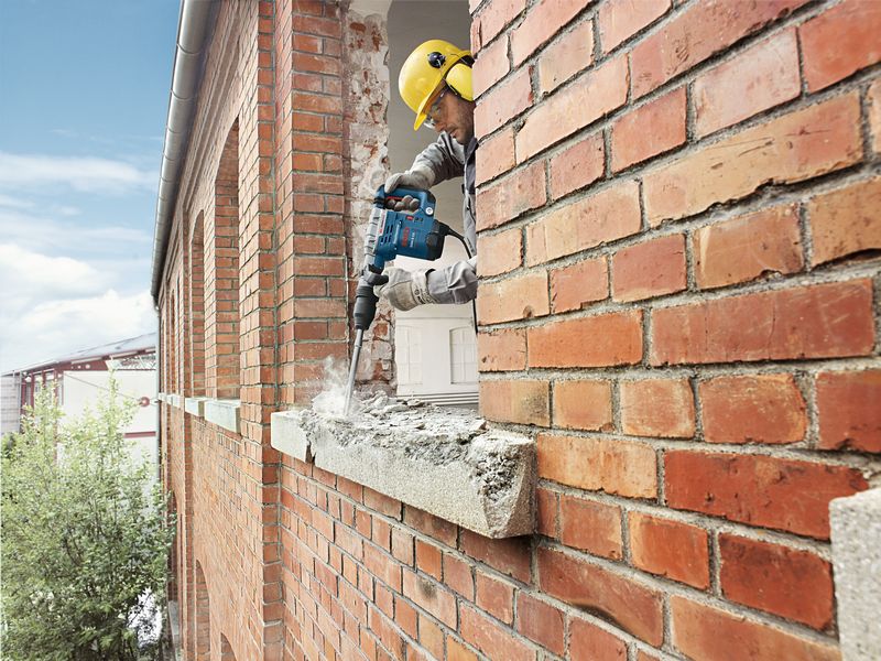 Eine Person mit Schutzausrüstung bohrt in einen gemauerten Fensterrahmen. Anwendungsbild