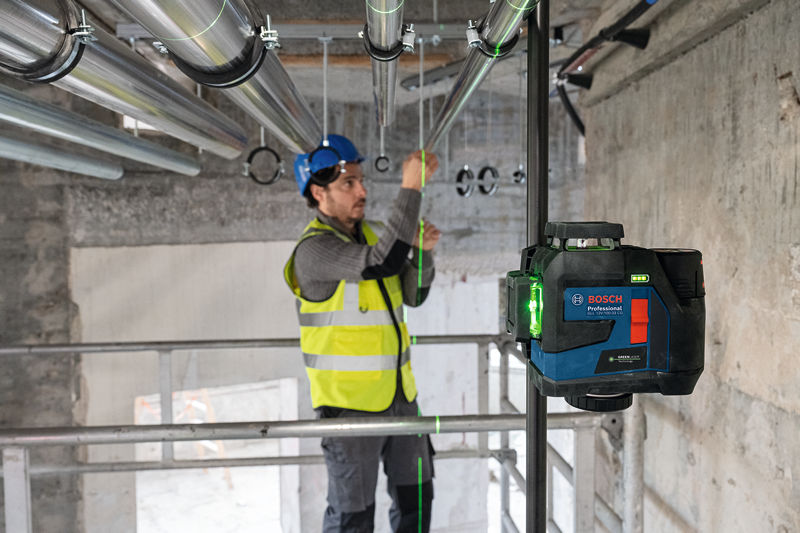 Eine Person mit Sicherheitsausrüstung richtet Metallrohre mit einem Lasernivelliergerät aus. Anwendungsbild