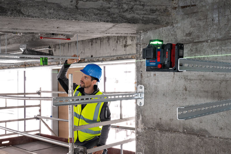 Eine Person mit Sicherheitsausrüstung richtet Metallstangen mit einem Lasernivelliergerät aus. Anwendungsbild