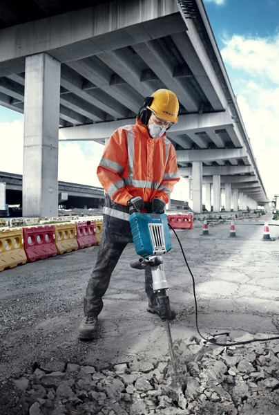Eine Person mit Sicherheitsausrüstung bricht im Freien mit einem großen elektrischen Hammer Beton auf. Anwendungsbild