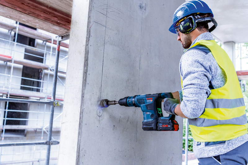 Person mit Schutzausrüstung bohrt mit Akku-Bohrhammer in eine Betonwand. Anwendungsbild