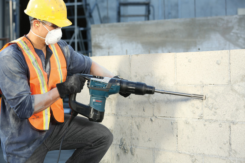 Eine Person mit Schutzausrüstung bohrt mit einem Bohrhammer in eine Betonwand. Anwendungsbild
