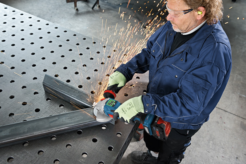 Eine Person mit Schutzausrüstung schleift mit einem Winkelschleifer einen Metallträger, wodurch Funken entstehen. Anwendungsbild
