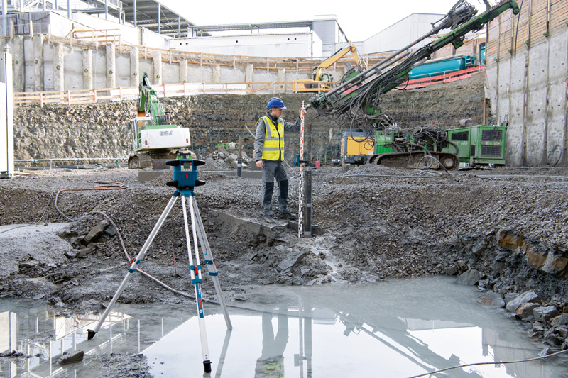 Eine Person mit Sicherheitsausrüstung verwendet auf einer Baustelle ein Lasernivelliergerät. Anwendungsbild