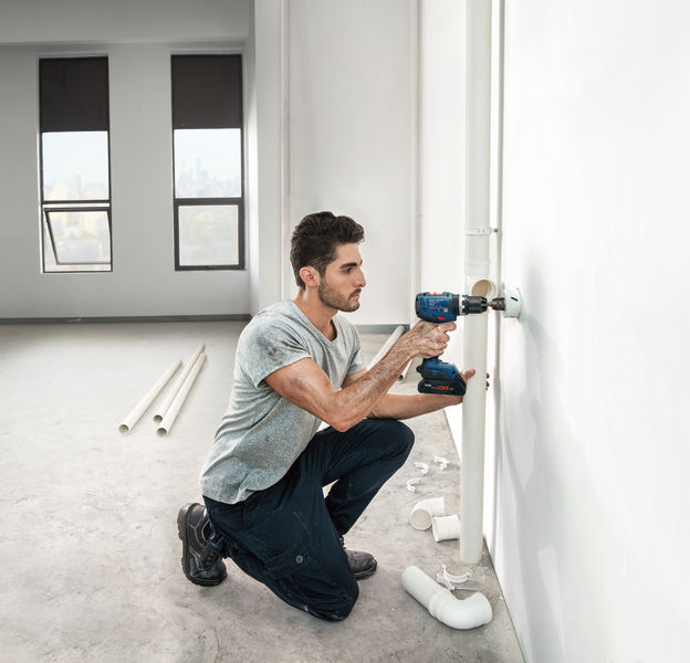 Eine Person bohrt in eine Wand, um in einem hellen, unfertigen Raum Rohrleitungen zu installieren. Anwendungsbild