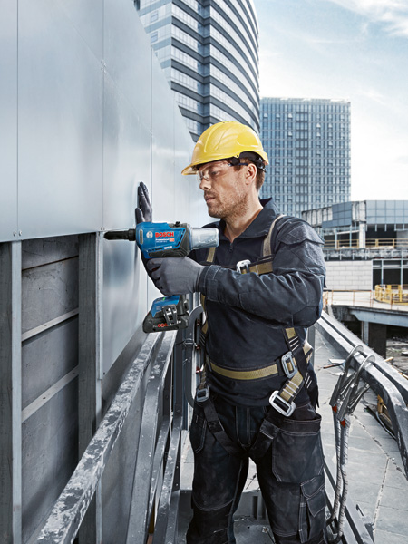 Eine Person mit Sicherheitsausrüstung befestigt Metallverkleidungen mit einer kabellosen Nietpistole. Anwendungsbild Weitwinkelaufnahme